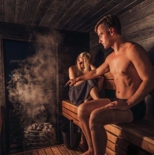 Mies ja nainen istuvat saunan lauteilla höyryisessä saunassa